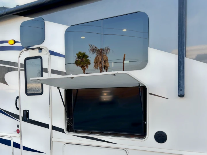 RV rental: Exterior view of an open TV compartment, revealing the screen, with palm trees reflecting in windows above.. Flair-Fleetwood Flair-Fleetwood Motorhome 2020