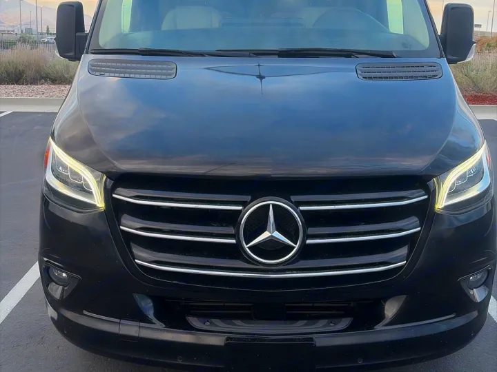 Head-on, sleek black Mercedes-Benz Sprinter van for RV rental. Bright LED headlights & chrome grille stand out.. Midwest Automotive Designs Ultimate RV 2023