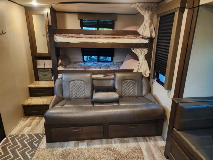RV rental interior: comfortable bunk beds, grey sofa with cup holders, and steps with storage. Ideal for travel.. Grand Design Transcend Xplor 2022