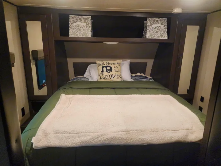 Cozy RV rental bedroom with a made bed, camping pillow, and overhead storage bins, ready for adventure.. Grand Design Transcend Xplor 2022