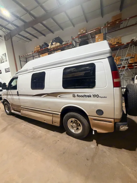 This white and tan Roadtrek 190 Popular RV camper van, great for **rv rental**, is seen indoors with a high top and spare tire.. Roadtrek Roadtrek Class B 2004