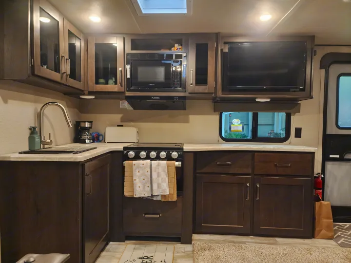 Well-equipped RV rental kitchen featuring a sink, stove, microwave, coffee maker, and TV, perfect for travel.. Grand Design Transcend Xplor 2022
