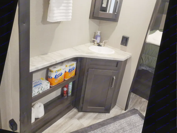 Compact RV rental bathroom with corner sink vanity, medicine cabinet, towel, and organized open shelving for bathroom essentials.. Grand Design Transcend Xplor 2022