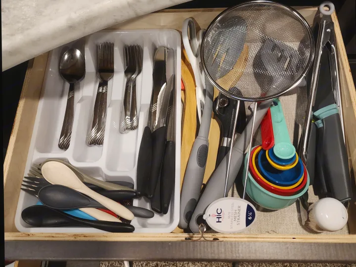 RV rental kitchen drawer neatly organized with cutlery, cooking utensils, colorful measuring cups, and a strainer.. Grand Design Transcend Xplor 2022