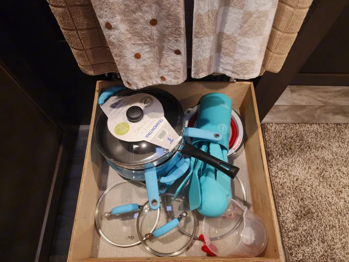 RV rental kitchen drawer with bright blue cookware, utensils, lids, and a measuring cup, showcasing compact organization.. Grand Design Transcend Xplor 2022