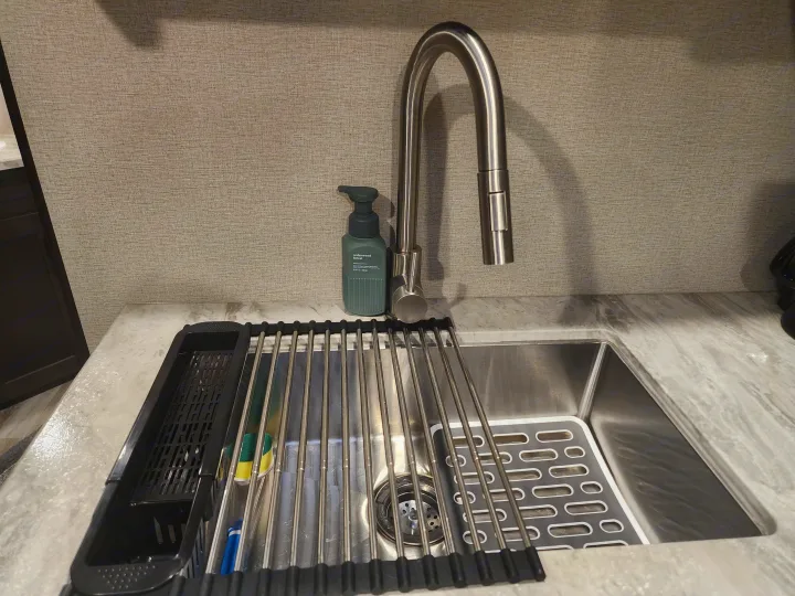 Modern RV rental kitchen sink area: stainless faucet, soap, roll-up dish rack, and marble-look counter.. Grand Design Transcend Xplor 2022