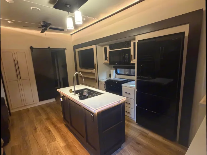 Spacious and modern RV rental kitchen featuring an island with sink, black appliances, ceiling fan, and barn doors.. Forest River Sabre 2025