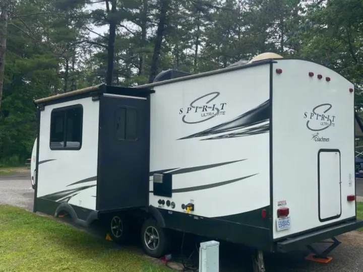 This RV rental is a white Spirit Ultra-Lite travel trailer by Coachmen, with an extended slide-out, parked at a wooded campground.. Coachmen Spirit 2019