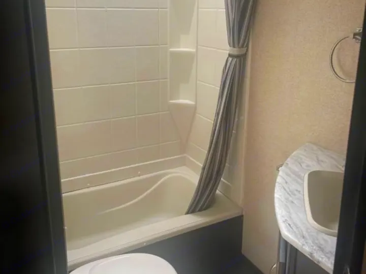 Compact RV rental bathroom with shower/tub, striped curtain, and sink, offering essential amenities in a small space.. Coachmen Spirit 2019
