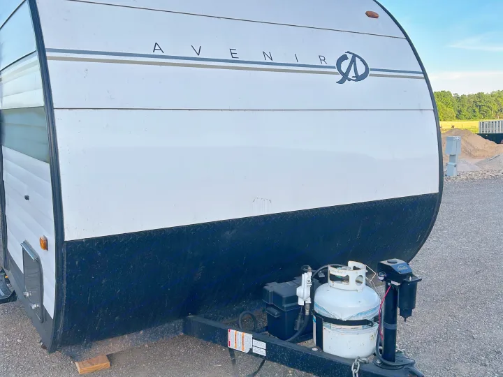 Front view of a white Avenir RV rental travel trailer with its propane tank and hitch assembly visible on a gravel lot.. Cruiser RV A-17BH Avenir 2024
