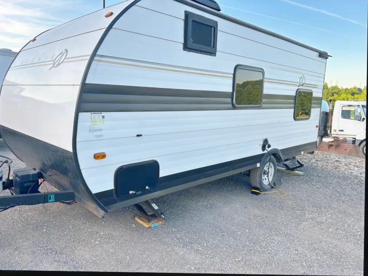 This white Avenir travel trailer RV rental, stabilized on gravel, features windows and a visible power cord for use.. Cruiser RV A-17BH Avenir 2024