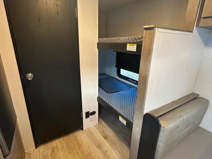 Inside this RV rental: a dark door, stacked bunk beds with mattresses & a window, plus floor outlets for your journey.. Cruiser RV A-17BH Avenir 2024