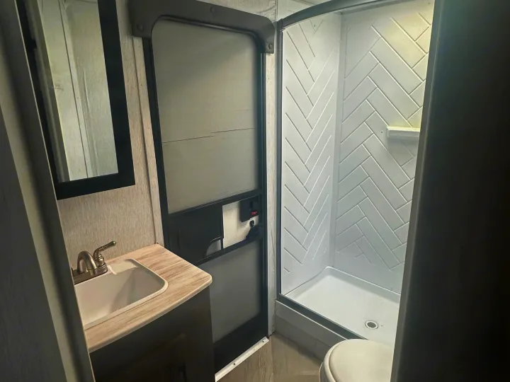 A bright, compact RV rental bathroom, featuring a vanity with sink, mirror, shower stall, and toilet, plus a ceiling skylight.. Forest River Salem Cruise Lite 2022