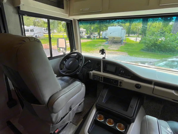 Inside this comfortable rv rental, the driver's seat and cockpit are visible, looking out onto a peaceful campground.. Flair-Fleetwood Flair-Fleetwood Motorhome 2022