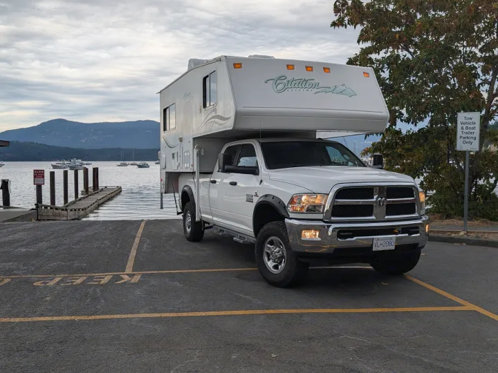 White truck camper (like an RV rental) at a BC boat launch. Scenic mountains & water make for a perfect outdoor adventure.. Dodge Dodge 1 Ton Pu 2014
