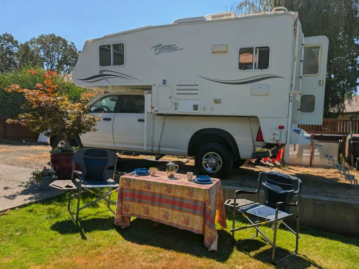 Outdoor dining by a Citation Supreme truck camper RV rental. A picnic table with chairs on the grass under a clear sky.. Dodge Dodge 1 Ton Pu 2014