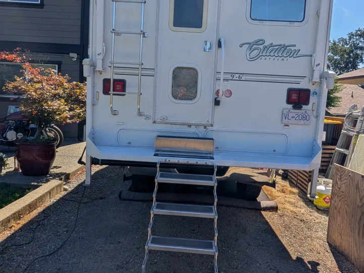 Rear view of a white Citation Supreme truck camper with portable steps, ideal for an rv rental adventure.. Dodge Dodge 1 Ton Pu 2014