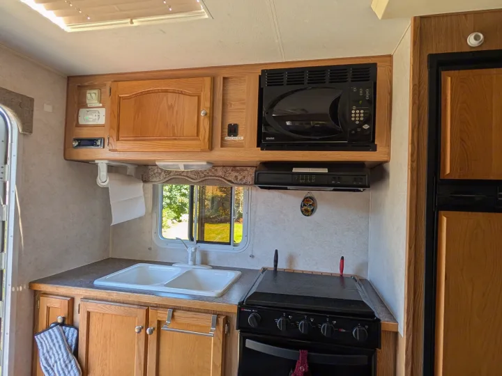 Inside an rv rental kitchen showing the dual sink, stove, microwave, and overhead cabinets for a comfortable trip.. Dodge Dodge 1 Ton Pu 2014