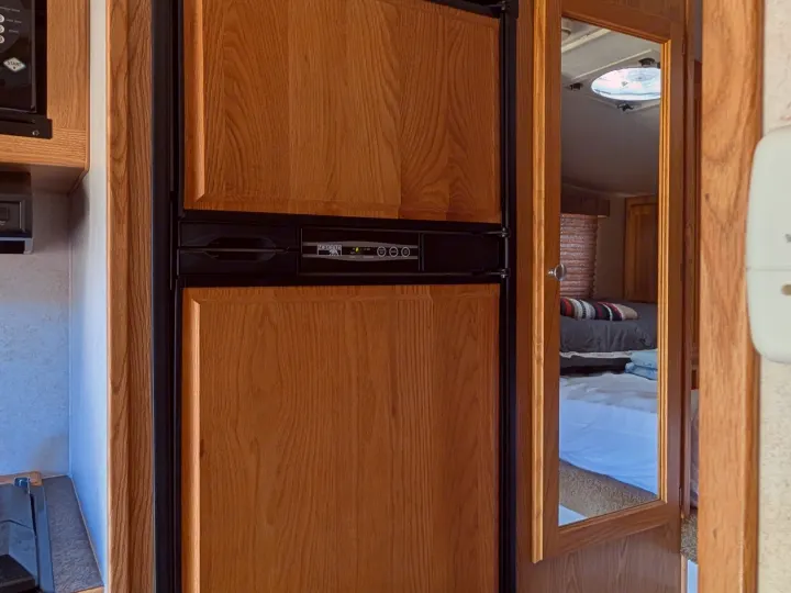 Interior of an RV rental with a wood-paneled refrigerator and a mirror reflecting a bedroom with a bed and ceiling vent.. Dodge Dodge 1 Ton Pu 2014