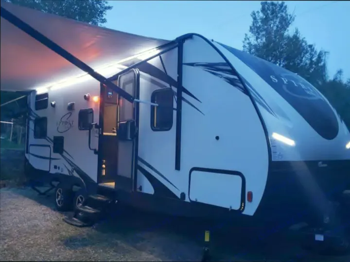 A white travel trailer rv rental, illuminated at dusk with an extended awning and interior lights, perfect for camping.. Coachmen Spirit ultra lite 2019