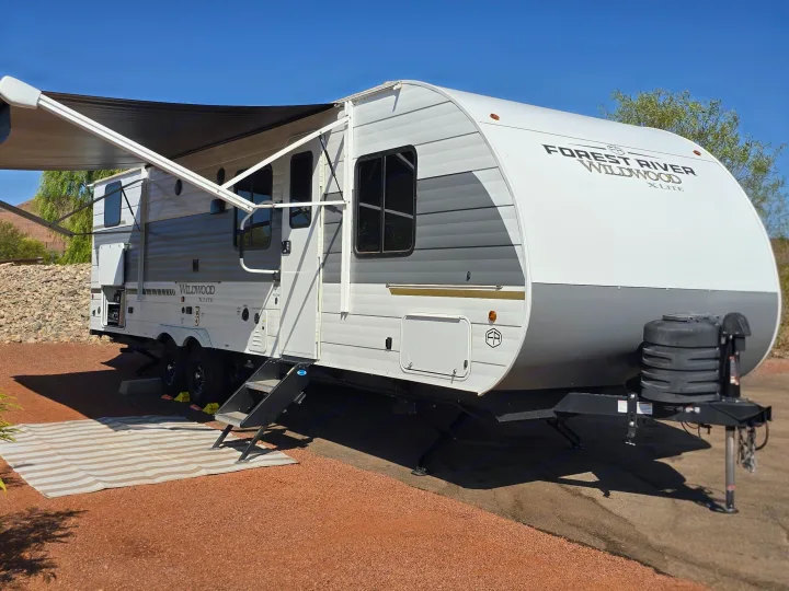 A white and gray Forest River Wildwood X-Lite rv rental, parked outdoors with its awning extended on a sunny day.. Forest River Wildwood X-Lite 2025