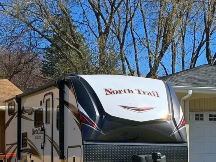 Front view of a white & black North Trail travel trailer, ideal for an RV rental, parked in a driveway under a bright blue sky.. Heartland RVs North Trail 2019