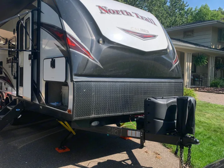 This North Trail Caliber travel trailer, a great RV rental option, is parked, showing its front, propane tanks, and side storage.. Heartland RVs North Trail 2019