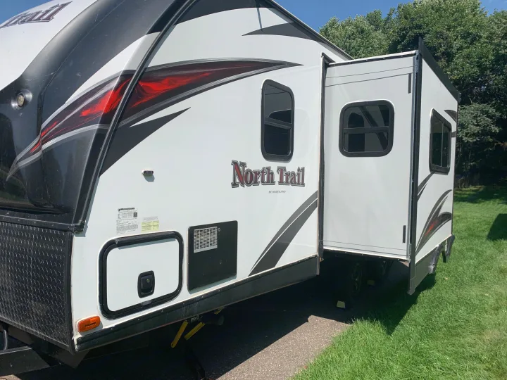 Side view of an RV rental: a white North Trail travel trailer with red/black graphics and an extended slide-out.. Heartland RVs North Trail 2019