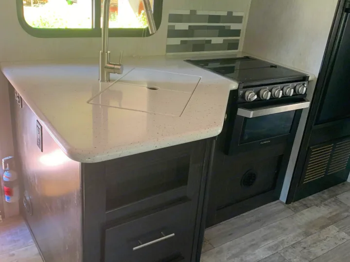 Modern RV rental kitchen showcasing a speckled countertop, sink, pull-down faucet, built-in stove/oven, and dark cabinetry.. Heartland RVs North Trail 2019