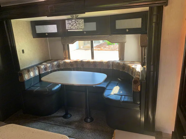 Cozy RV rental dinette featuring U-shaped booth seating, an oval table, overhead cabinets, and a window view.. Heartland RVs North Trail 2019