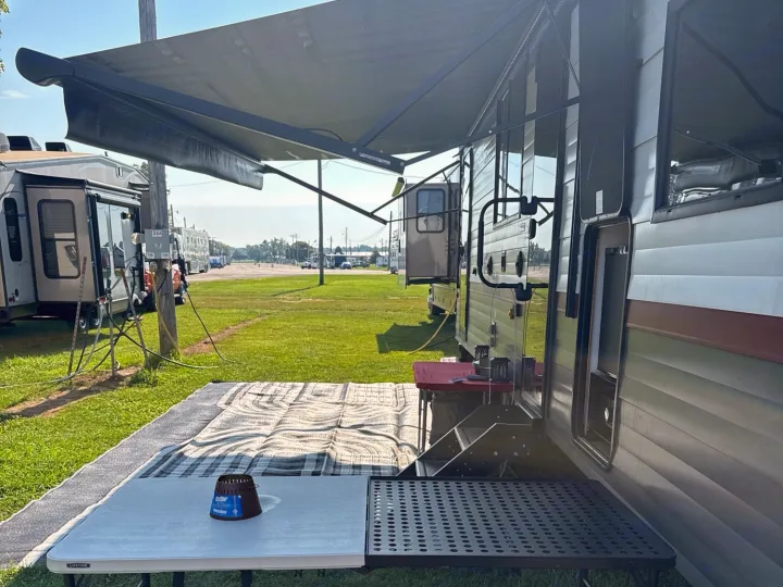 RV rental parked at a sunny campsite with an extended awning, outdoor mat, and tables, perfect for leisure.. Forest River Campsite Reserve 2025