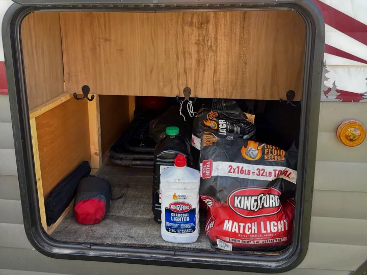 RV rental storage stocked with Kingsford charcoal, lighter fluid, and camping gear, ready for outdoor cooking.. Forest River Campsite Reserve 2025