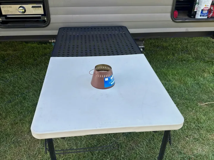 RV rental site: outdoor folding tables and a lantern, with camping gear visible in the trailer's storage compartments.. Forest River Campsite Reserve 2025