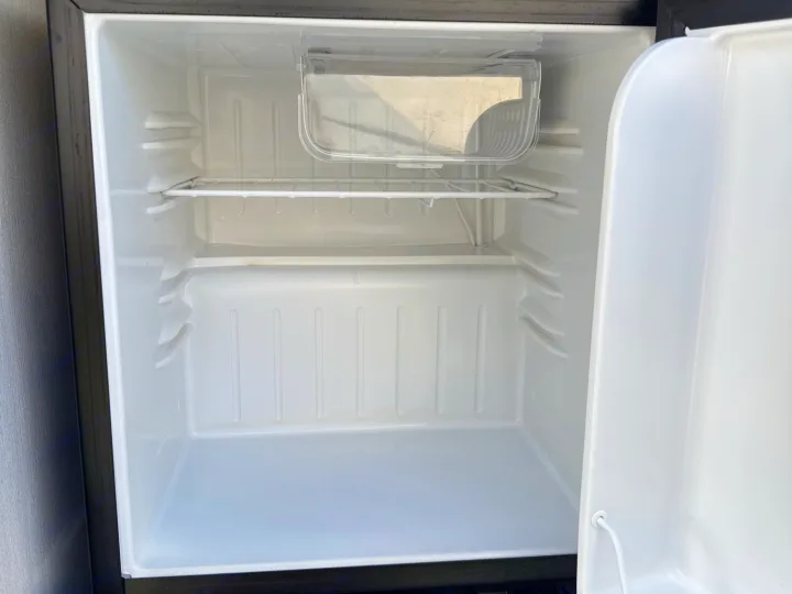 Inside a clean, empty mini-fridge in an RV rental, featuring a wire shelf and small clear compartment.. Forest River Campsite Reserve 2025