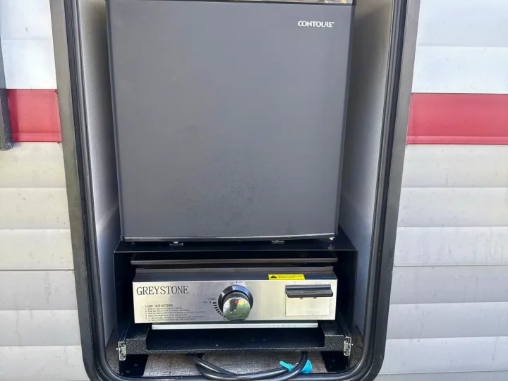 An RV rental's outdoor kitchen: a Contoure mini-fridge and Greystone griddle ready for camp cooking.. Forest River Campsite Reserve 2025