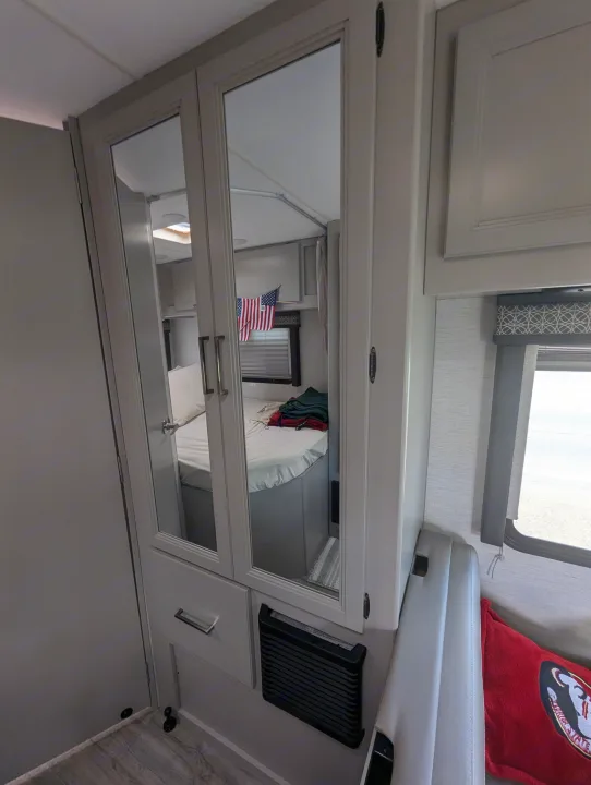 Modern RV rental interior: Mirrored closet doors reveal the bedroom with a neatly made bed and an American flag.. Thor Quantum SE 2025