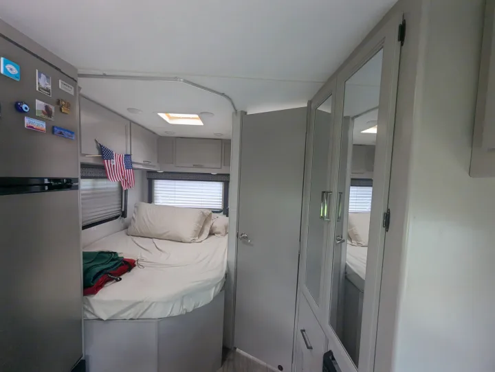 Cozy rv rental interior: a compact bedroom with bed, small fridge, overhead cabinets, and mirrored closet doors.. Thor Quantum SE 2025