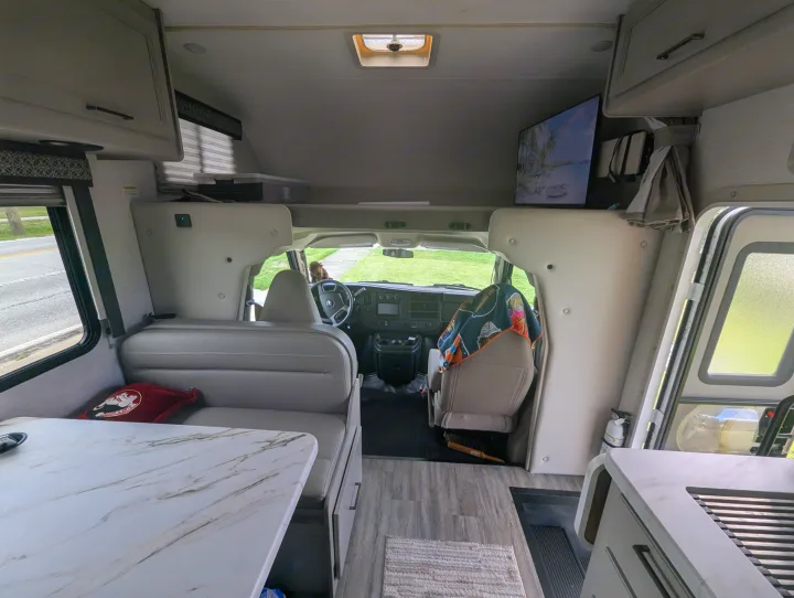 RV rental interior featuring a dinette, cockpit, overhead bed, and kitchen area, with a roadside view outside.. Thor Quantum SE 2025