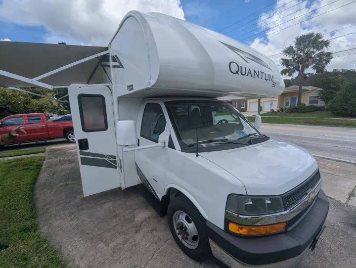 Spacious white Class C RV rental with its awning extended and door open, ready for your next road trip.. Thor Quantum SE 2025