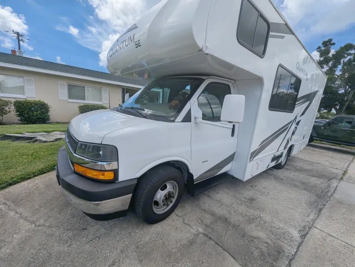 White Quantum SE Class C RV rental parked on a driveway, showing its front, side, and over-cab bunk.. Thor Quantum SE 2025