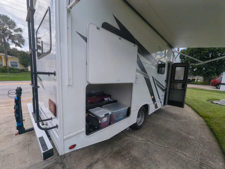 RV rental with its rear storage compartment open, showing bins inside. The awning is extended & front door open.. Thor Quantum SE 2025