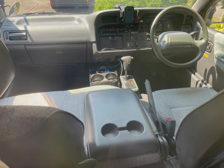 Inside an rv rental, showing the front cabin with dashboard, steering wheel, automatic shifter, and console with cup holders.. Toyota Hiace Campervan 1994