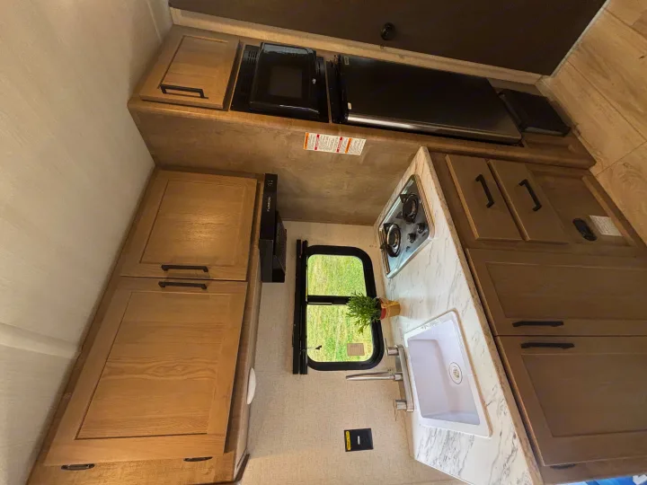 Compact RV rental kitchen features a sink, two-burner stove, microwave, and wooden cabinets. Ideal for road trip cooking.. Keystone RV Springdale 2025