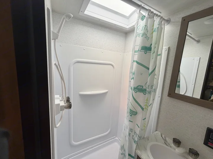 Inside an RV rental bathroom, featuring a clean shower with a patterned curtain, sink, and mirror. Compact and functional.. Keystone RV Springdale 2025