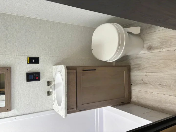 Clean and functional RV rental bathroom with a white toilet, vanity with sink, and shower area, all in light tones.. Keystone RV Springdale 2025