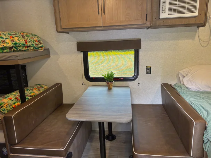 Cozy RV rental interior with dining booth, bunk beds, and a main bed. Features overhead cabinets and an AC unit for comfort.. Keystone RV Springdale 2025