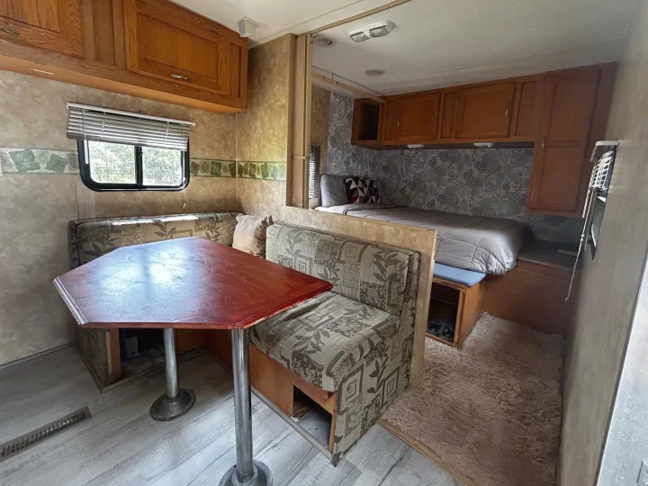 Cozy RV rental interior: dinette with patterned seats, wood table, and adjacent bed area with overhead cabinets.. Coachmen Spirit of America 2009