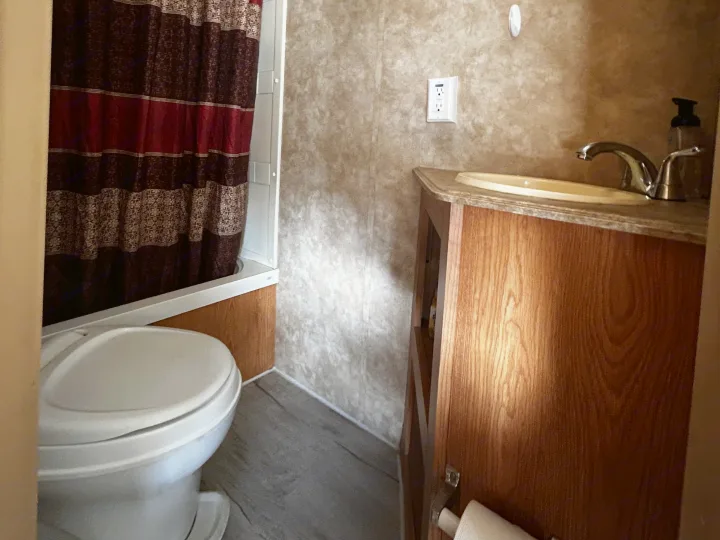 Bathroom of an RV rental with toilet, tub/shower, sink, and wood vanity. Includes a patterned curtain and USB outlet.. Coachmen Spirit of America 2009