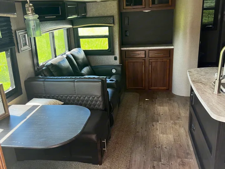 Modern RV rental interior featuring a dinette, leather couch, kitchen area, and bright windows with green views.. Jayco Eagle HT 2020