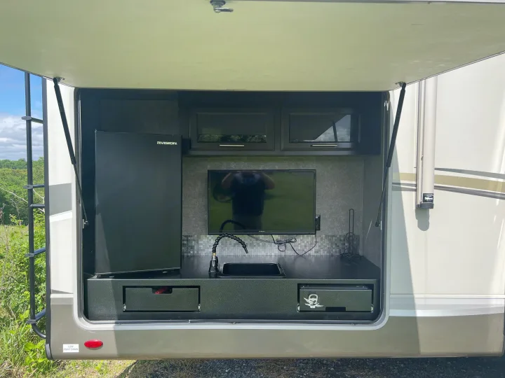 An RV rental's outdoor kitchen and entertainment setup, complete with a fridge, TV, sink, and storage cabinets.. Jayco Eagle HT 2020